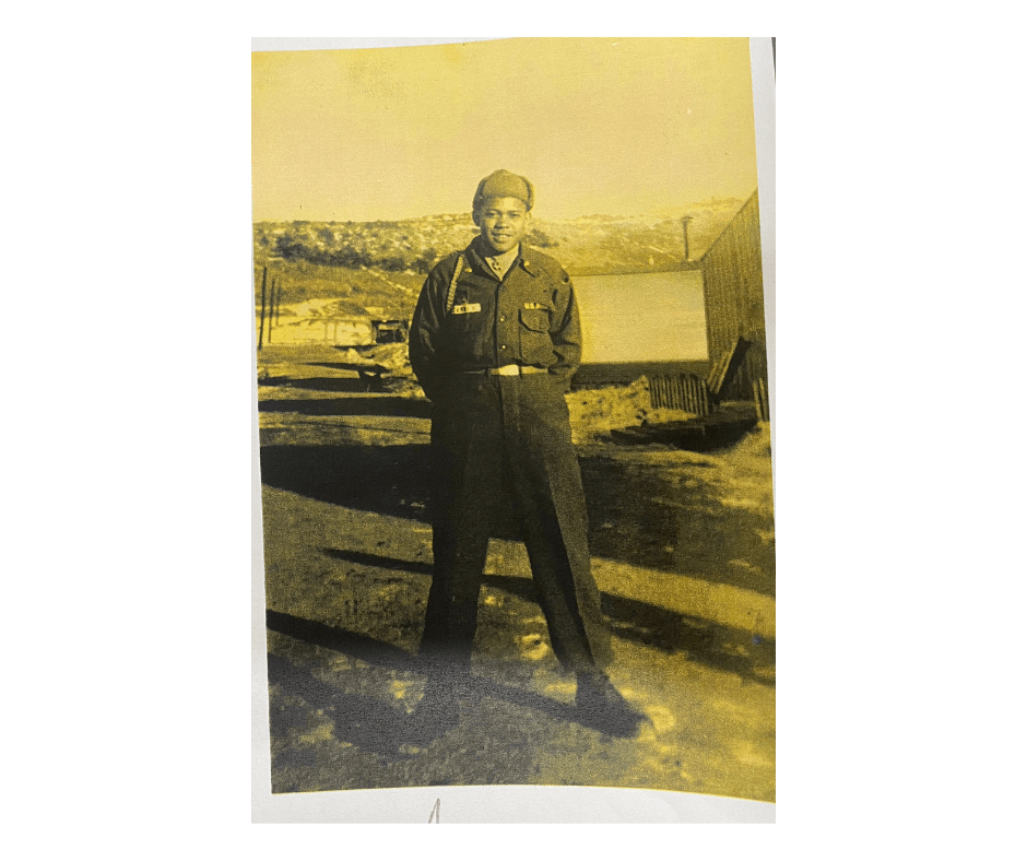 Posing soldier in uniform smiling into camera with army base behind him