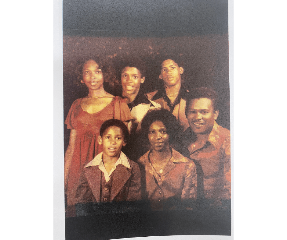 Family portrait of six people. Mother and dad sit on the right with one son next to them, while three older children stand behind them.