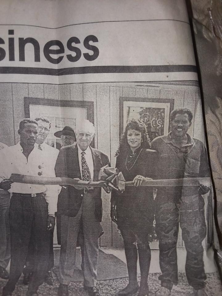 Clipping of newspaper business section. Four people stand in front of ribbon for an opening ceremony of businesses.