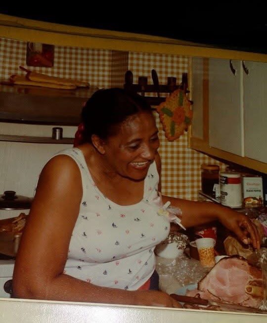 Smiling woman in kitchen standing beside counter where ham is being cut
