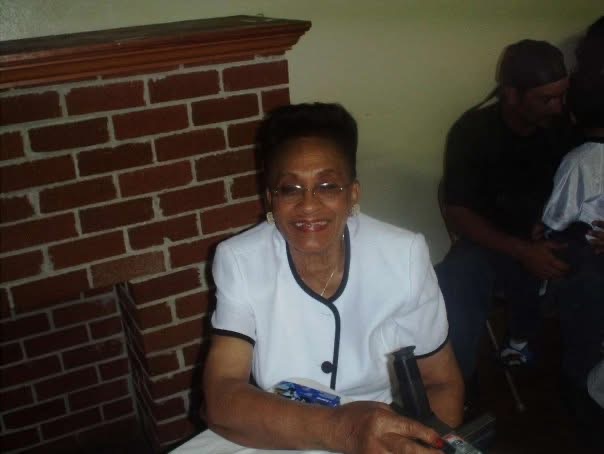 Smiling woman in a white and black dress sitting in front of brick fireplace 