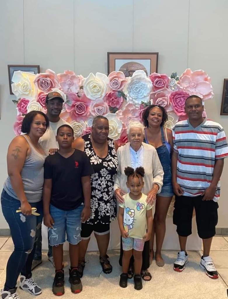 family photo of eight people in front of a pink rose backdrop