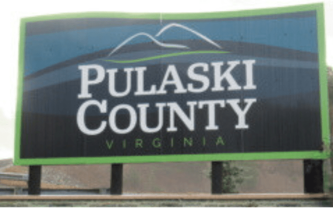 Road billboard with text 'Pulaski County, Virginia'. Mountains are depicted with line drawings above text.