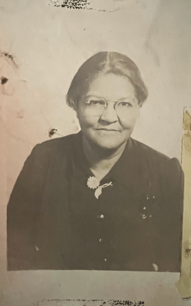 Black and white photograph of an older woman wearing glasses and a black blouse sitting for a portrait