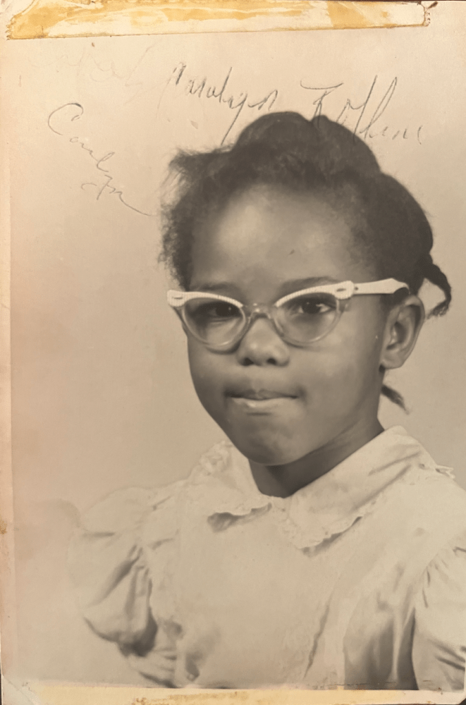 Black and white portrait of a young girl with pursed lips wearing glasses and a collared shirt