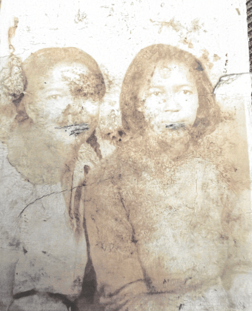 Deeply weathered portrait of two women sitting next to one another with blank expressions.
