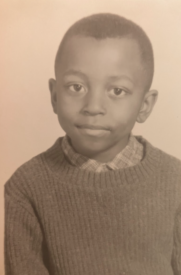 Black and white photo of a young boy wearing a u-neck sweater with a flannel underneath with a softly smiling for a portrait