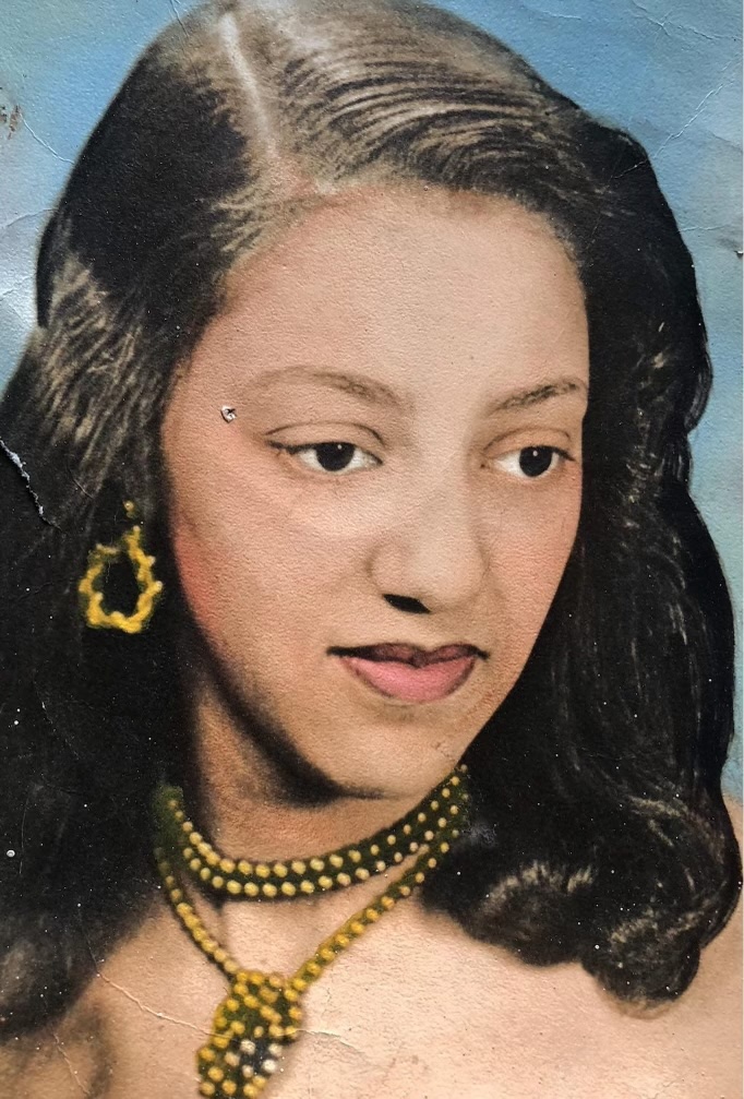 Portrait with vivid coloring that features a woman gazing down and to the right. Her hair is curled and is cascading down to her shoulders. She is wearing a gold beaded necklace and gold hoop earrings.