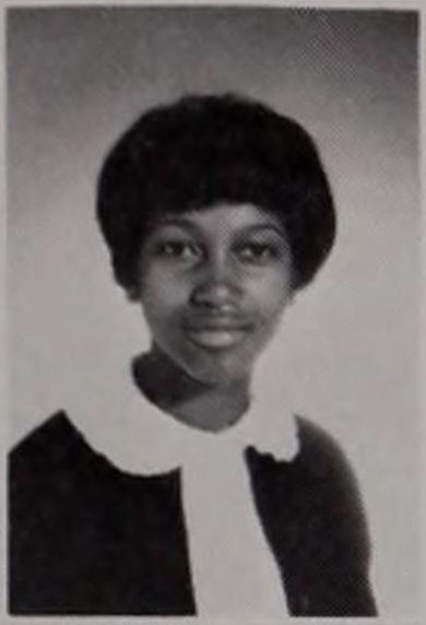 Black and white yearbook photo of a young girl wearing a sweater and a collared shirt gently smiling. 